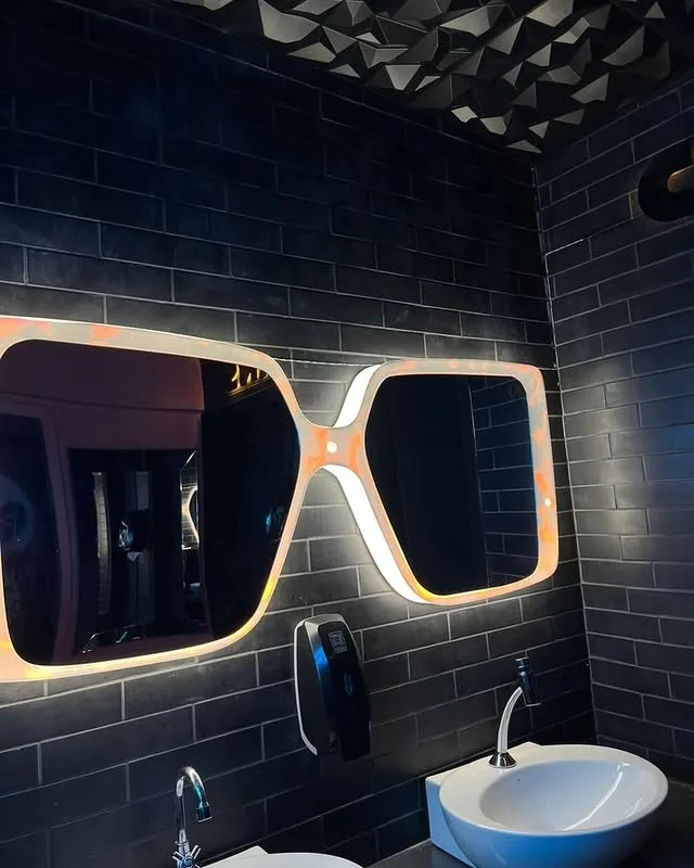 Banheiro com porta rosa, espelho retroiluminado e letreiro em néon