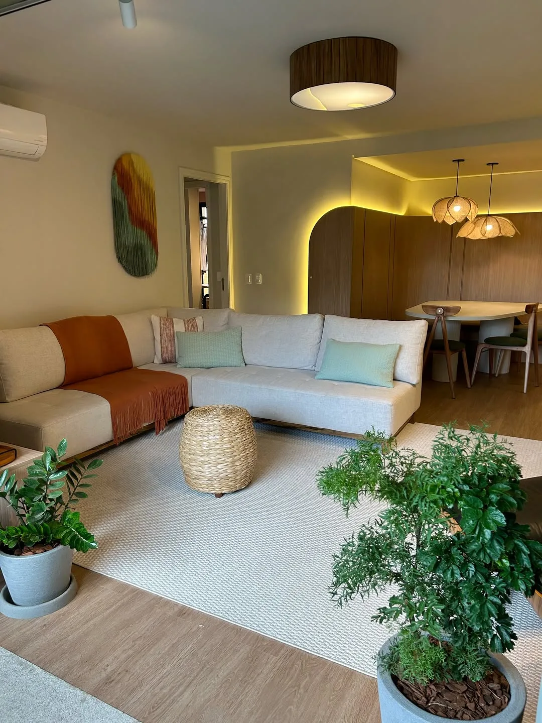 Sala de estar com arco de marcenaria contornado por fita de luz quente, sofá claro e vegetação junto à janela