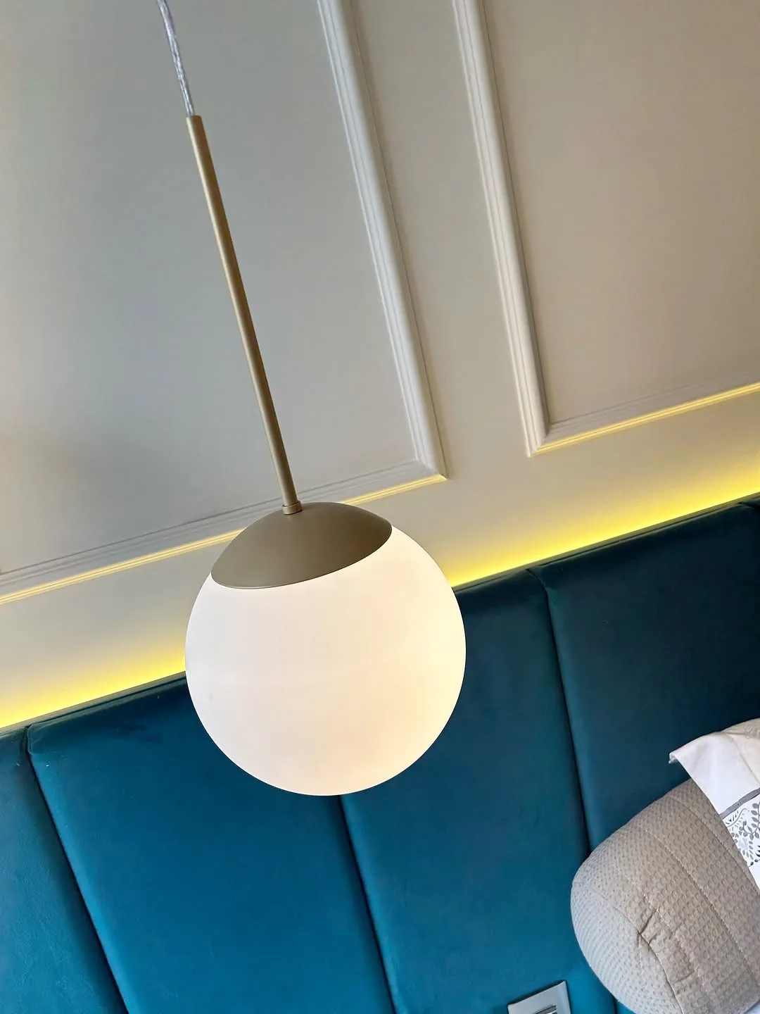 Detalhe de pendente esférico sobre painel estofado em verde petróleo, com fita de luz na borda superior