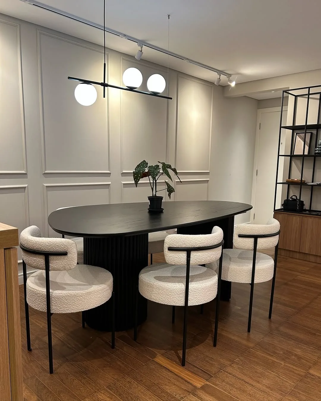 Sala de jantar com mesa oval preta, cadeiras estofadas claras e pendente linear com globos de vidro