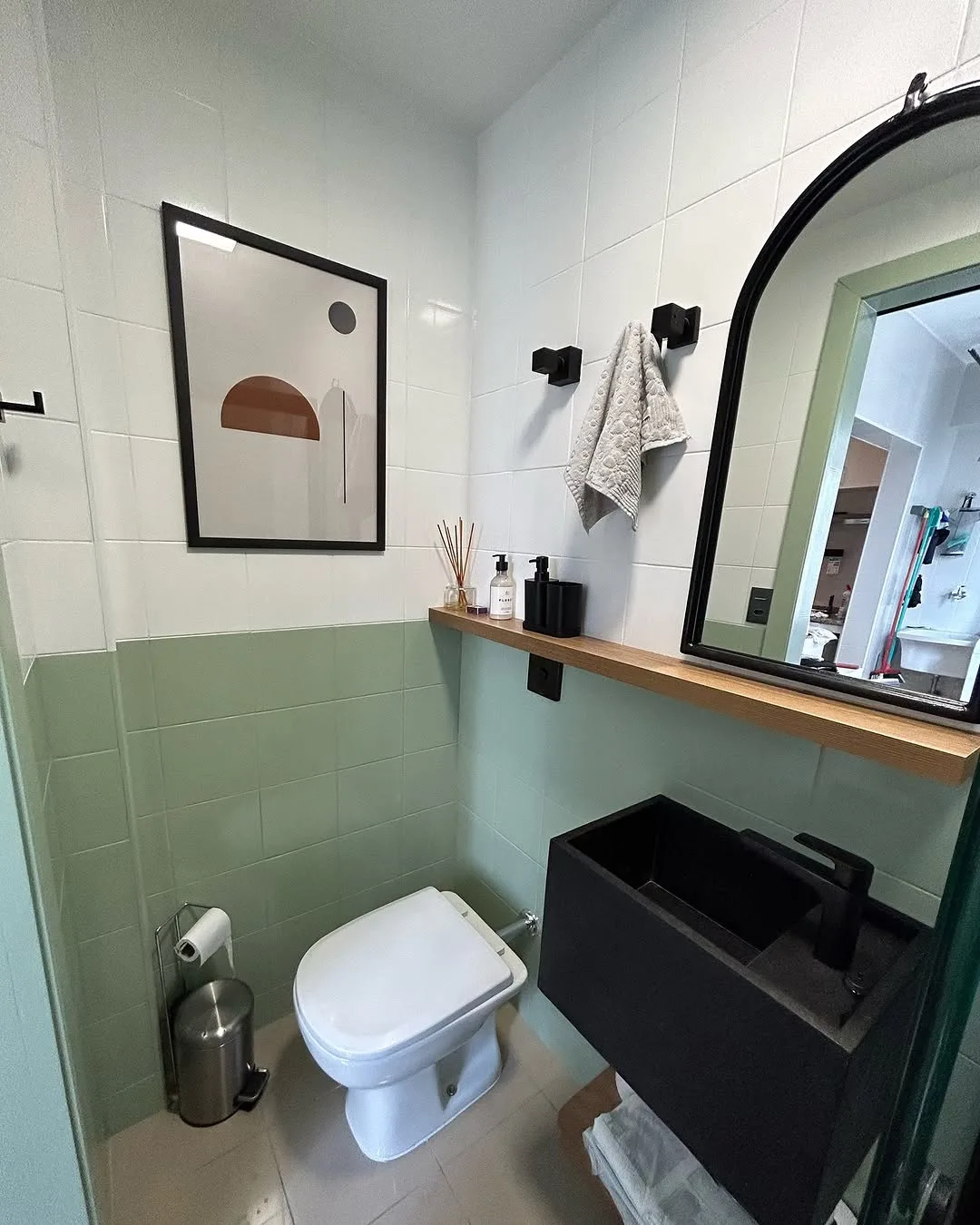 Lavabo com parede verde-sálvia, espelho arqueado de moldura preta e prateleira de madeira