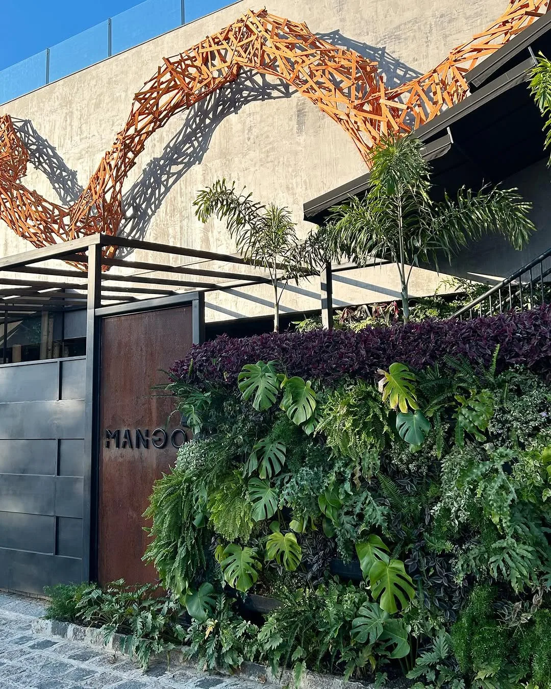 Fachada do Mango com parede verde viva e arco de metal corten
