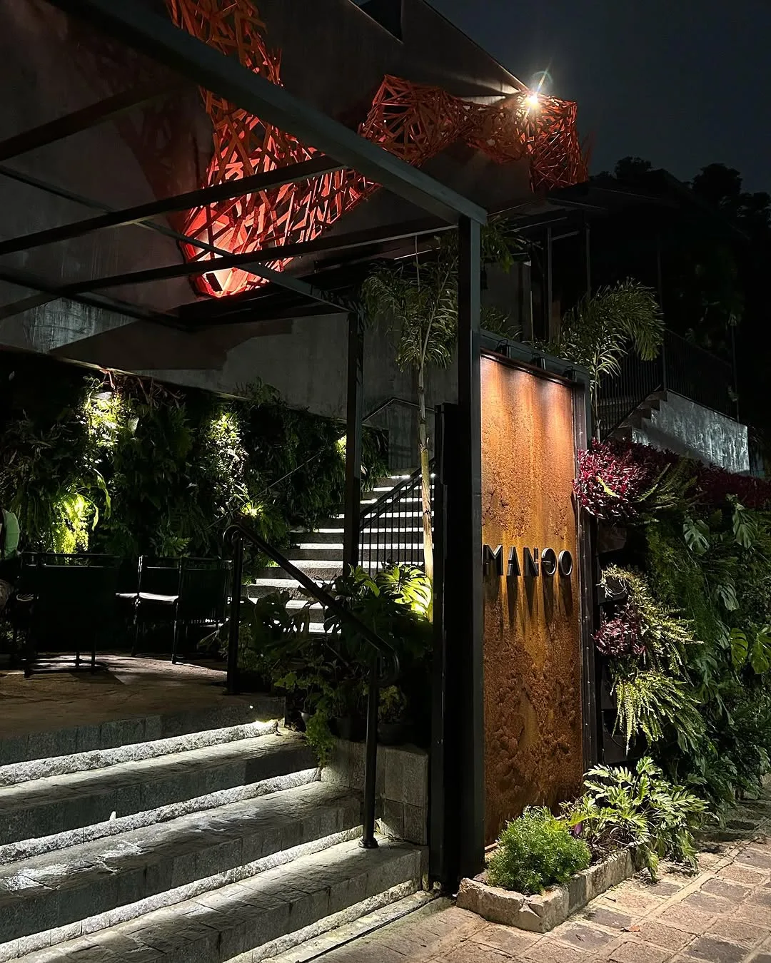 Entrada do Mango à noite, com painel perfurado iluminado em laranja