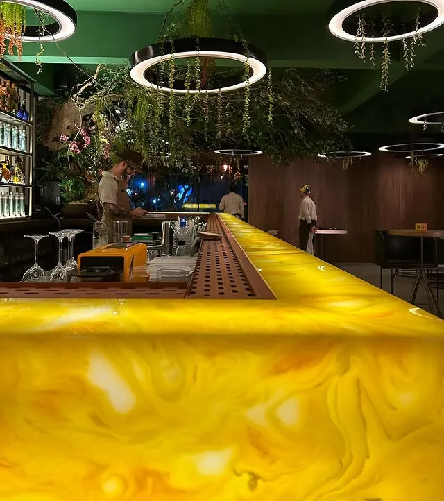 Balcão de bar em ônix amarelo retroiluminado, brilhando de dentro, sob uma fileira de anéis de luz