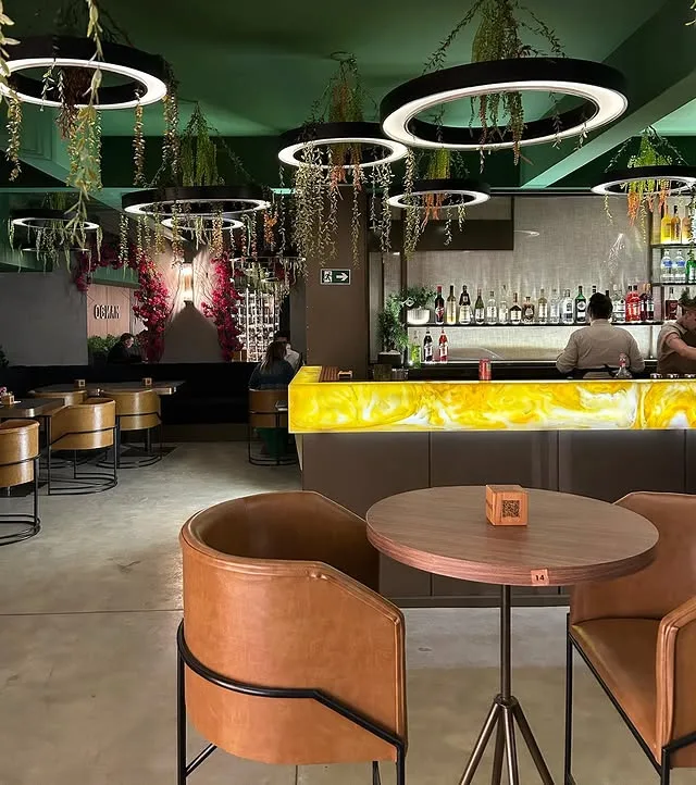 Salão visto do bar, com o balcão de ônix aceso e os anéis de luz alinhados no teto