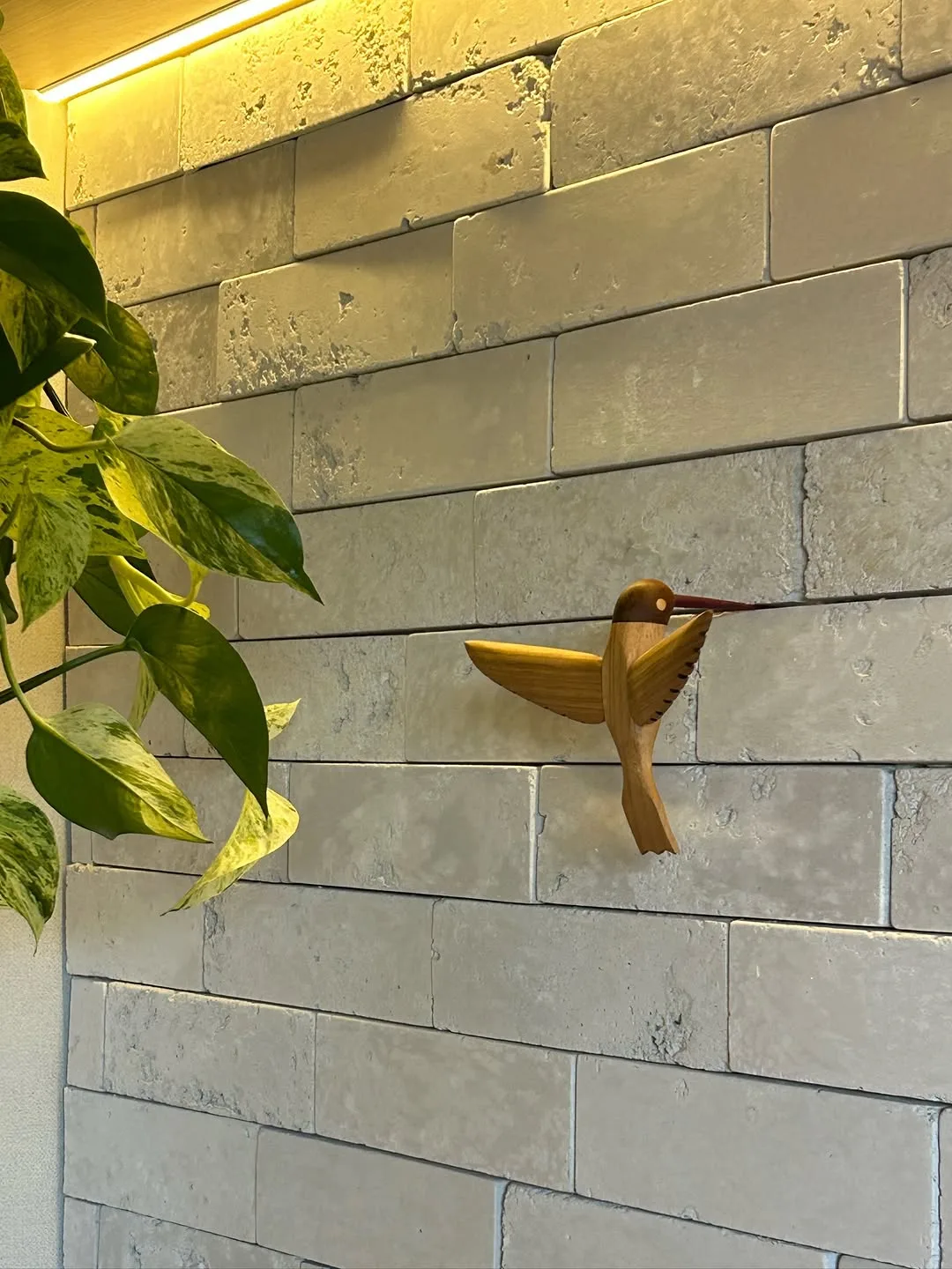 Estar com parede verde-sálvia e tijolo branco, poltrona de couro preto, plantas e fita de luz amarela no forro