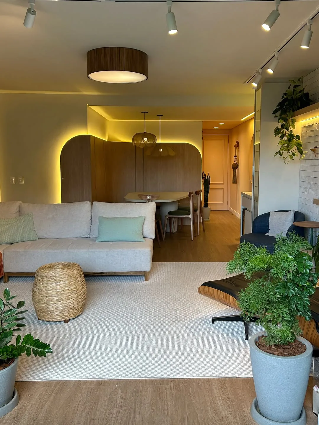 Ambiente de estar com tijolo branco, plantas suspensas e iluminação em trilho