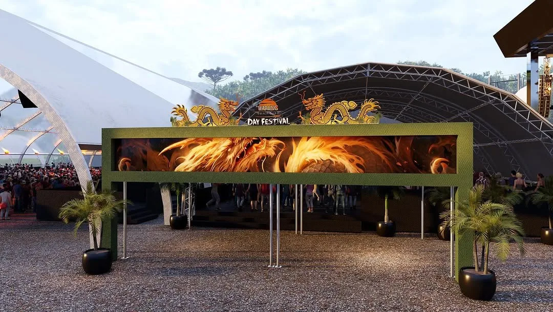 Interior da estrutura com treliça vermelha, mesas comunitárias e fogo central